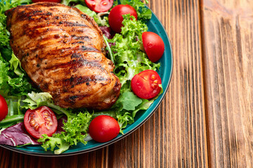 Grilled chicken breast ( fillet ) with lattuce salad and cherry tomatoes . Top view
