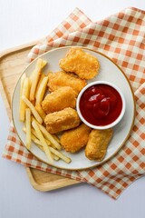 Fried chicken nuggets with french fries and tomato sauce in a ceramic plate on white background table, top view food table