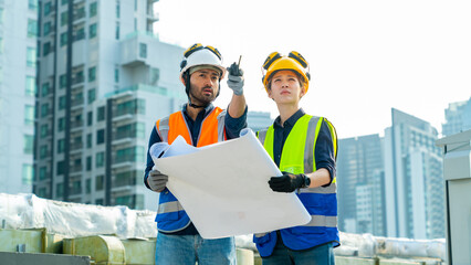 Professional Asian man and woman teamwork engineer and foreman using blueprint working outdoor at construction site building rooftop. Architecture inspector inspect building exterior structure system.