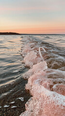 Sunset at lake with waves forming pink ribbon shape on shore
