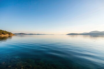 Tranquil lake reflecting a serene blue sky and distant hills