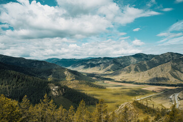 Obraz premium A breathtaking view of green valleys and rugged mountains under a bright blue sky creates a stunning landscape in the Altai Mountains