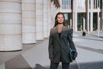Professional woman confidently standing outside modern office buildings, holding a tablet. Her...