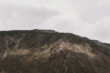 The Altai Mountains rise dramatically, their rugged slopes illuminated by soft sunlight breaking through the clouds at dawn