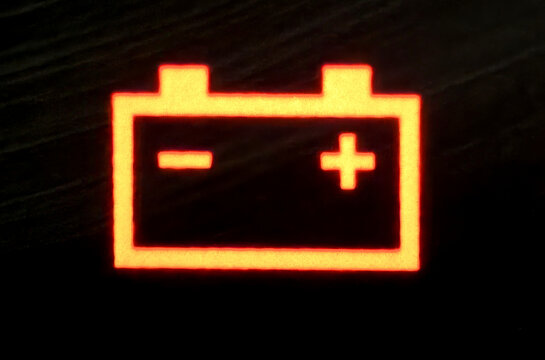 An extremely close-up picture of a battery light signal glowing on the dashboard.