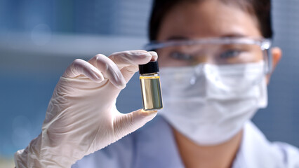 A light yellow vial featured in the center of photo frame by female scientist, over blurred...