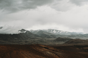 The Altai Mountains display dramatic clouds hovering over their peaks, creating a tranquil ambiance in the breathtaking landscape