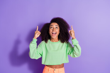 Portrait of smiling cheerful young curly girl wearing green top and mini skirt index fingers up...