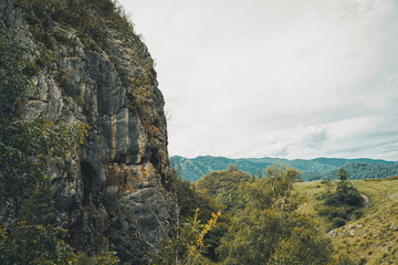 Towering cliffs rise above vibrant greenery under an expansive sky in the breathtaking Altai...