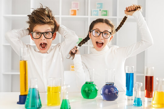 Two enthusiastic children in a chemistry class experimenting with colorful liquids in beakers. The kids show excitement and curiosity, embodying fun and learning in a school science lab.
