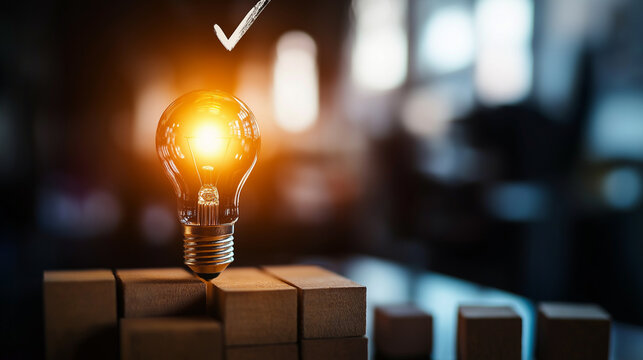 A glowing light bulb set on wooden blocks, with a checkmark overhead, conveying the notion of an innovative idea that has achieved success