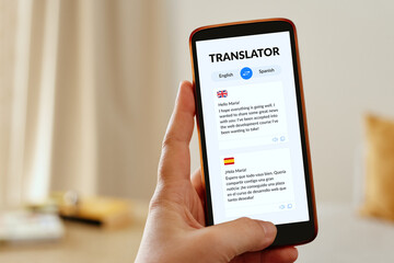 Female hand holding a mobile smartphone displaying a language translator app. 