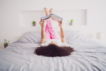 Fototapeta premium Full body photo of young attractive woman lying upside down bed read book wear stylish pajama soft comfy bedroom white room interior inside