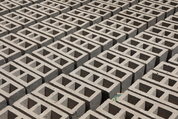 Rangées de parpaings creux gris en ciment, formés de trois alvéoles, et séchant sur le sol. Matériaux de construction constitués de blocs alignés formant une surface rugueuse. Photo prise au Sénégal.