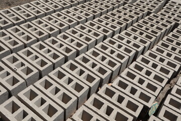 Rangées de parpaings creux gris en ciment, formés de trois alvéoles, et séchant sur le sol. Matériaux de construction constitués de blocs alignés formant une surface rugueuse. Photo prise au Sénégal.