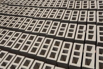 Rangées de parpaings creux gris en ciment, formés de trois alvéoles, et séchant sur le sol. Matériaux de construction constitués de blocs alignés formant une surface rugueuse. Photo prise au Sénégal.