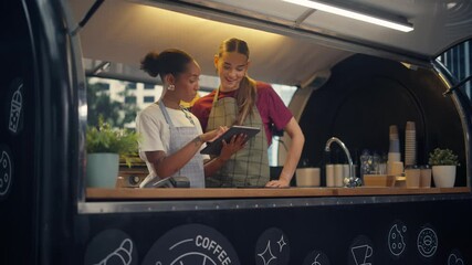 Two Female Food Truck Staff Members Having a Conversation while Using a Tablet Computer. Administrator and Barista Discussing Online Orders, Planning a Profitable Promotion on the Internet