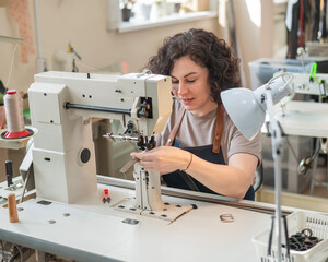 A woman tanner sews a leather belt on a sewing machine. 