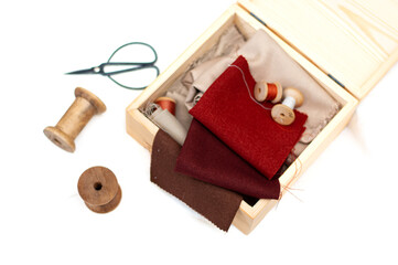 Samples of terracotta and red fabric, wooden reels for threads, scissors on a white background.