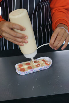 Woman hand squeezes mayonnaise on sausage bun