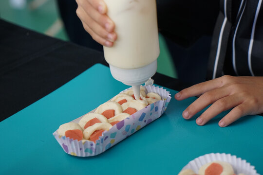Woman hand squeezes mayonnaise on sausage bun