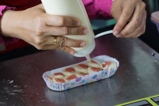 Woman hand squeezes mayonnaise on sausage bun