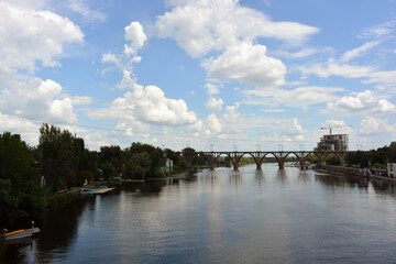 Beautiful view of the wide and long blue Dnipro River. Landscapes, a gray brick embankment with green trees, new construction sites and a beautiful bridge in the city of Dnipro.