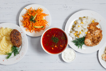 group photo of homemade food top view, salad, grilled chicken breast with rice, red soup, fried meat ball with mashed potato on a white wooden background