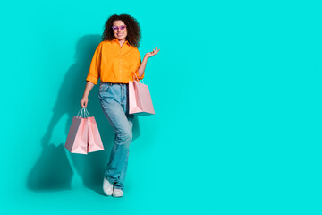 Full size photo of cool positive woman dressed orange shirt holding shopping bags near empty space...