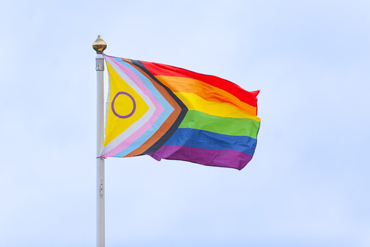 Progress Pride flag on flag pole in front of blank sky