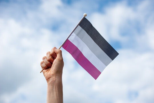 Hand holds up asexual pride flag against sky