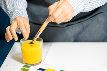 Artist rinsing out paintbrush with water in glass, close up