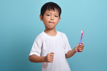 A happy Asian boy holding a toothbrush isolated on blue background. Boy smiles showing his teeth. Children's dental care and hygiene
