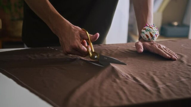 Cropped shot of unrecognizable male tailor cutting on garment at table while working on new fashion collection