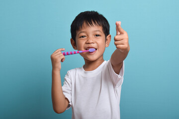 A happy Asian boy with clean teeth is brushing his teeth while pointing at the camera. Isolated on...