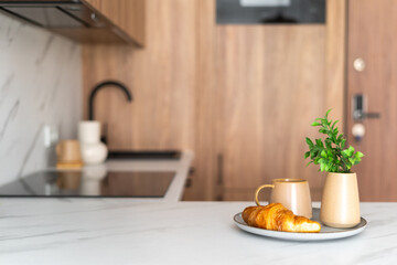 A cozy kitchen setting with a croissant, coffee, and a plant on a marble countertop