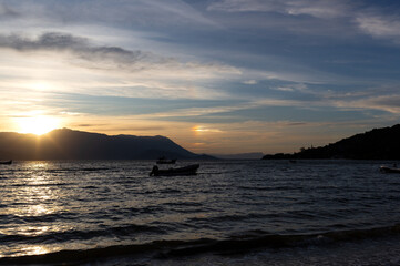 Golden sunset over calm waters, silhouetted boats, and serene mountains in the distance