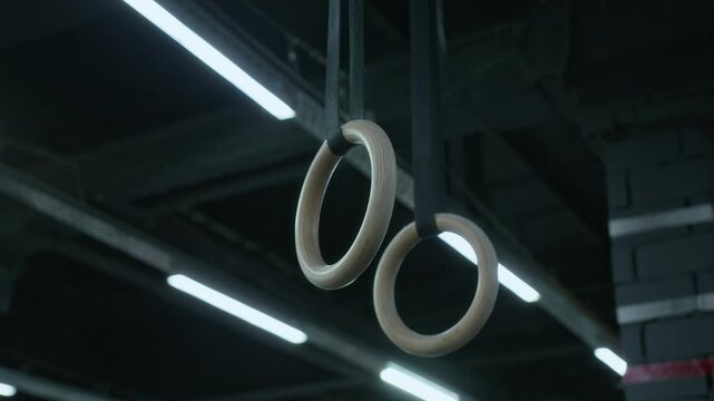 Tilt down no people shot of two wooden gymnastic rings hanging from gym ceiling