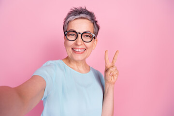 Portrait of nice aged lady selfie v-sign blue t-shirt isolated on pink color background