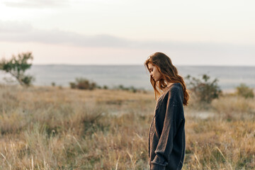 Solitary woman standing in vast field, gazing into distance as sun sets on the horizon