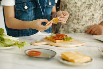 Close-up of girl making sandwich with cheese and tomatoes for breakfast in the kitchen