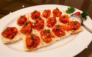 close up of many pieces of Chinese or Shanghai style sweet and sour sauce shrimp prawns on crispy rice crackers on a white plate