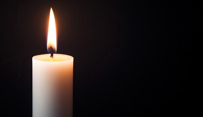 A burning candle shining against a dark background