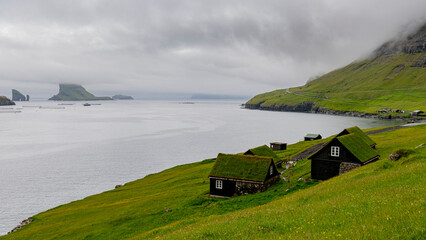 Paisaje de casas feroeses y vistas de Drangarnir ,entre las islas de V&aacute;gar y  el islote Tindh&oacute;lmur en Islas Faroe, un dia de niebla y lluvia fina de Julio