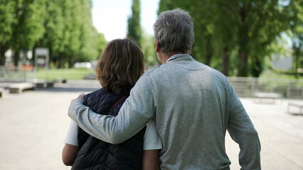 Obraz premium Elderly couple walking together in park, arm in arm, enjoying nature, surrounded by lush green trees, rear view, serene and peaceful atmosphere, outdoor leisure, senior companionship and love