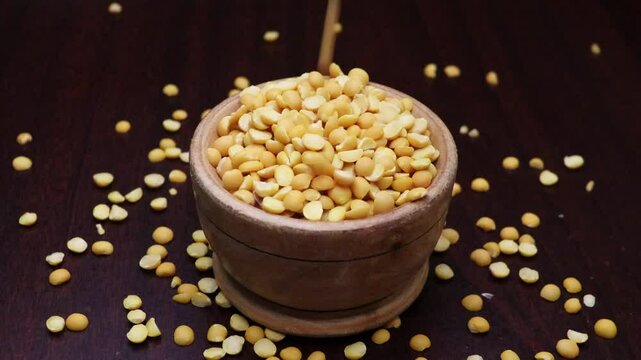 Pigeon pea legume or Arhar-toor dal are poured on a heap of wooden bowl 4k footage. yellow split lentils drops on the cup. Slow motion. 

