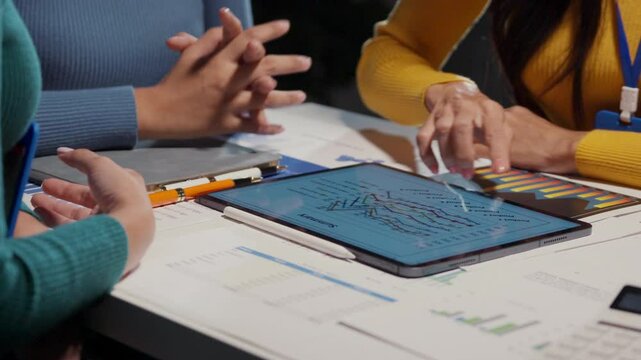 Businesswomen discussing financial data while analyzing information displayed on a tablet. Engaging in a collaborative meeting, they focus on charts and graphs to drive strategic decisions