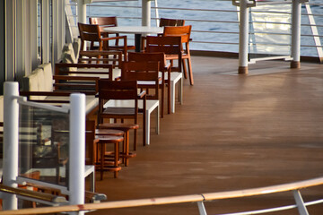 Outdoor seats on passenger ship deck with the calm seascape. Cruise ship deck. Wooden promenade deck on a luxury cruise liner. Ocean in background.