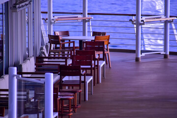 Outdoor seats on passenger ship deck with the calm seascape. Cruise ship deck. Wooden promenade deck on a luxury cruise liner. Ocean in background.