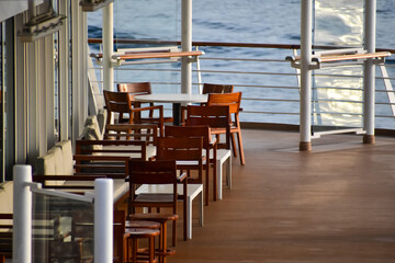 Outdoor seats on passenger ship deck with the calm seascape. Cruise ship deck. Wooden promenade deck on a luxury cruise liner. Ocean in background.